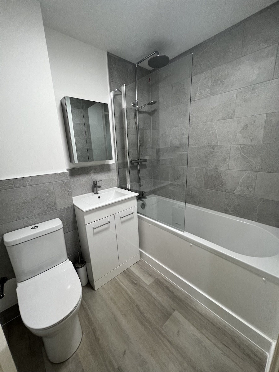 Grey tiled bathroom with bath and shower screen